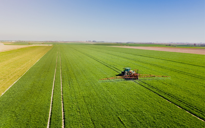 industrial agriculture, tractor spraying crop in huge field